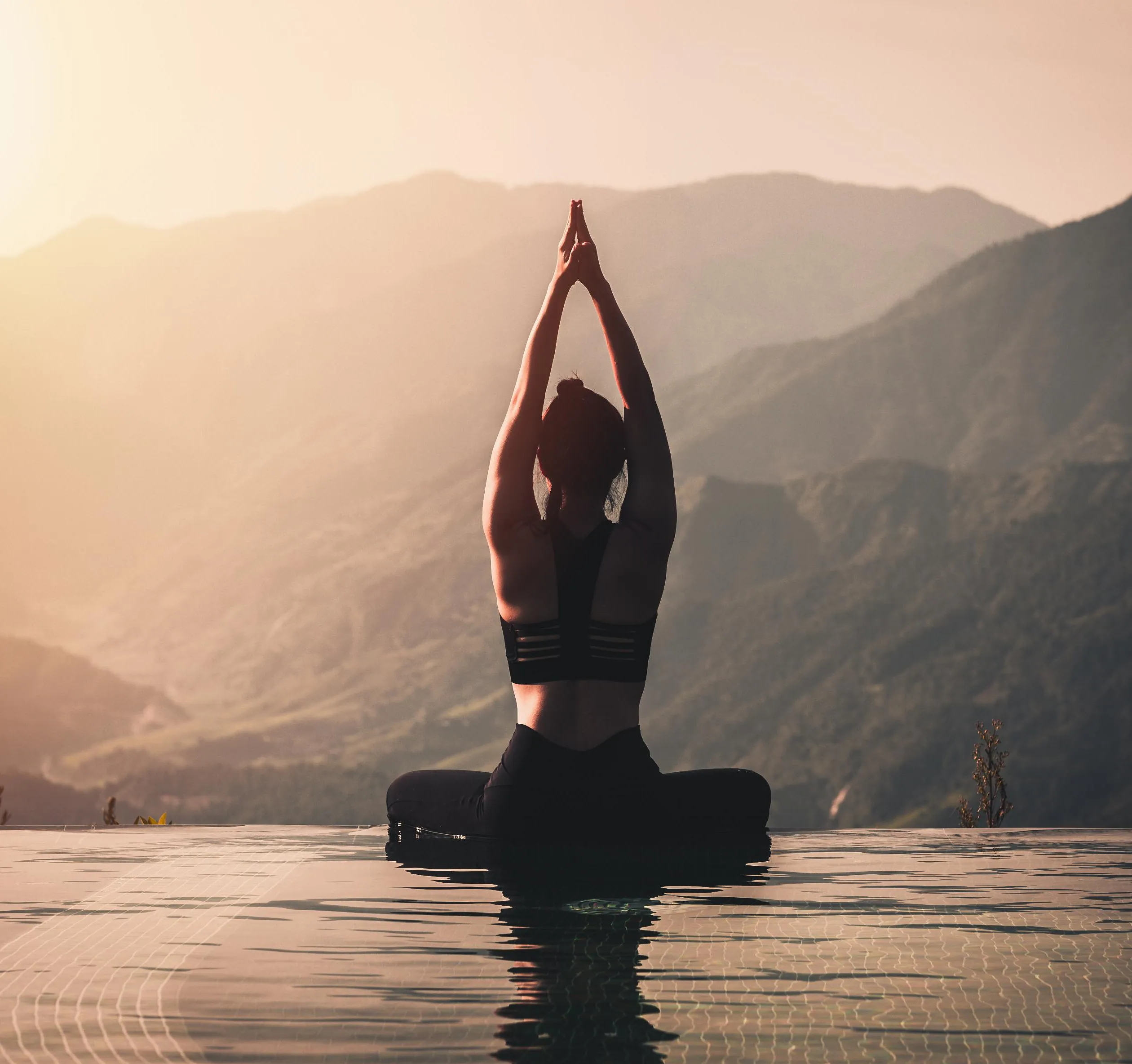 Kvinne i yoga stilling ved bassengkant, fjell i solnedgang bak.